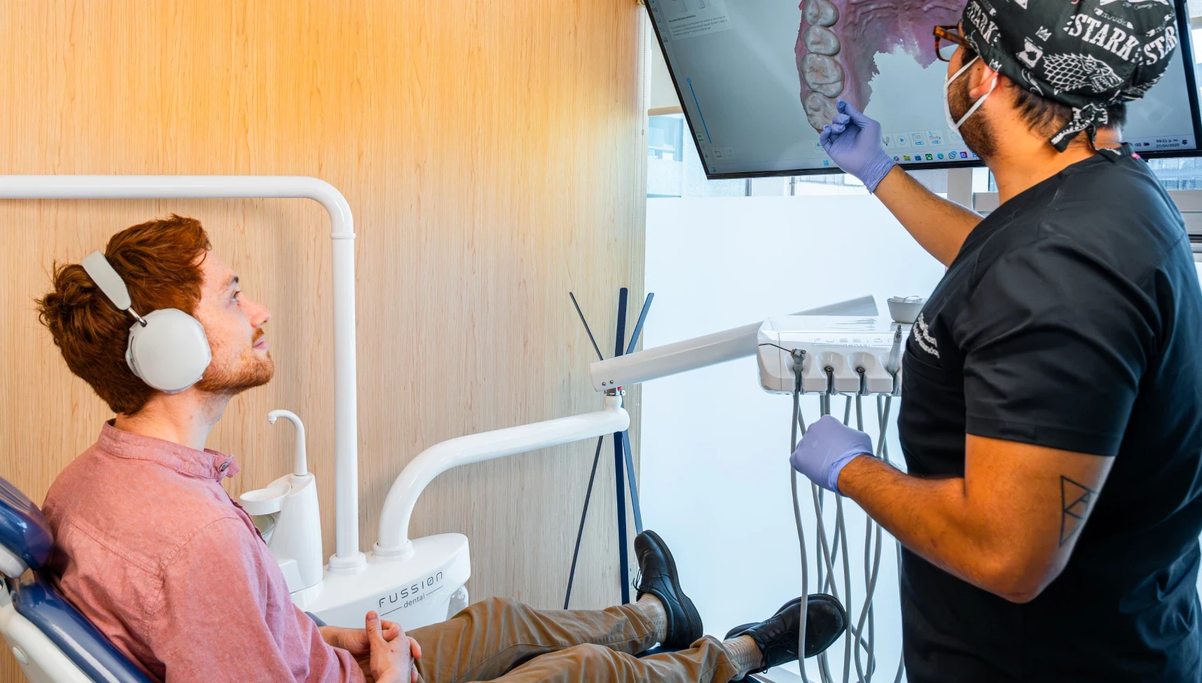 Dentist showing a 3D dental scan on a screen while the patient watches from the chair.